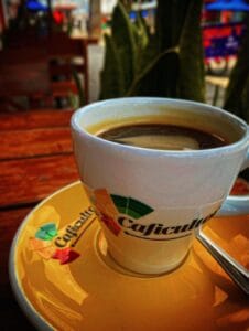 Primer plano de una taza de café caliente en un plato amarillo, con el logo de 'Caficultor' en la taza y el plato.