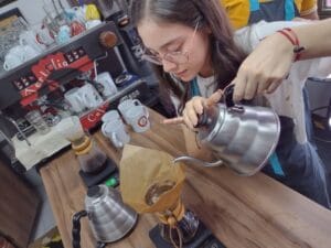 Joven barista con gafas preparando un café filtrado con una cafetera Chemex sobre una báscula