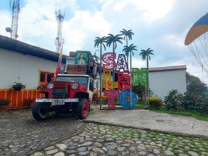 Un letrero de Salento junto a un Jeep Willys tradicionalmente cargado, capturando la esencia cultural y turística del Eje Cafetero.