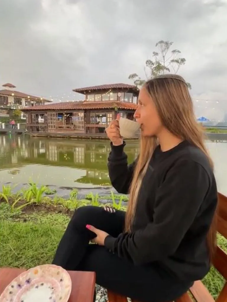 Mujer disfrutando de una taza de café de origen con vista a un lago y arquitectura rústica, experiencia en mirador de Salento, Quindío.