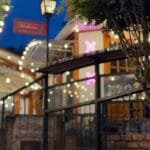 foto nocturna de El Patio Café Restaurante en Salento Quindío, con luces , fachada rústica, y un letrero de neón en forma de mariposa. Ambiente cálido y mágico en la Calle Real