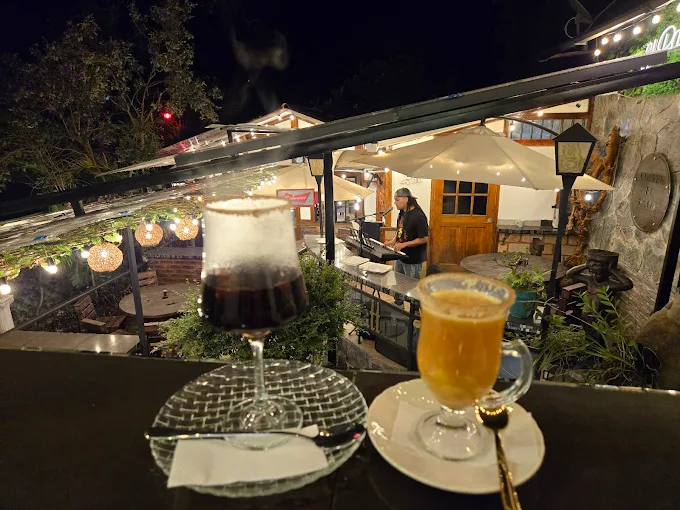 Vista nocturna de la terraza de El Patio Café Restaurante con dos copas en primer plano y un músico tocando un teclado, ambientado con luces cálidas de feria. Ambiente romántico y de ocio en Salento