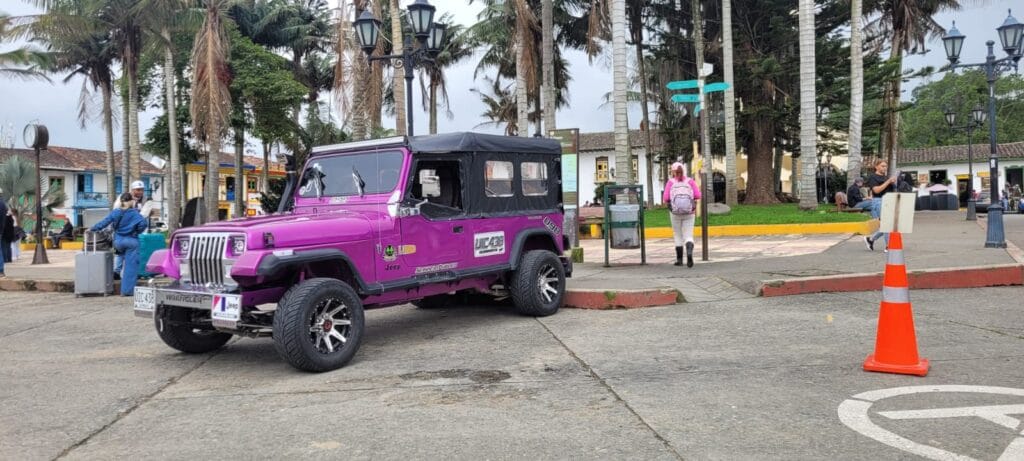 Un Jeep Willys de color magenta, icónico del transporte del Eje Cafetero, estacionado en la Plaza de Salento, Quindío.