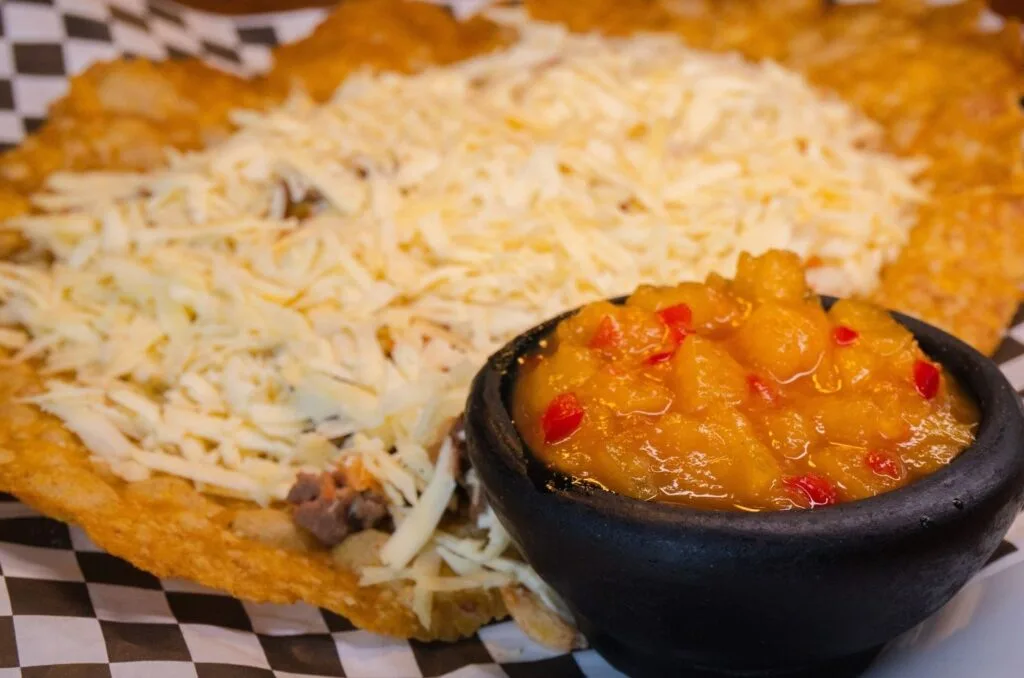 Patacón gigante crujiente, cubierto con queso fresco campesino y hogao (salsa de tomate y cebolla), un acompañamiento típico de Salento, Quindío.