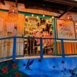 Vista de la entrada del Restaurante La Martina, mostrando una colorida pared exterior con un mural paisajístico, una baranda azul y la decoración floral y luminosa del interior visible a través del acceso