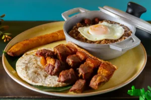 Plato típico de Filandia con calentado de frijoles servido en olla de aluminio, chicharrón crocante, arepa blanca, plátano maduro frito y huevo frito.