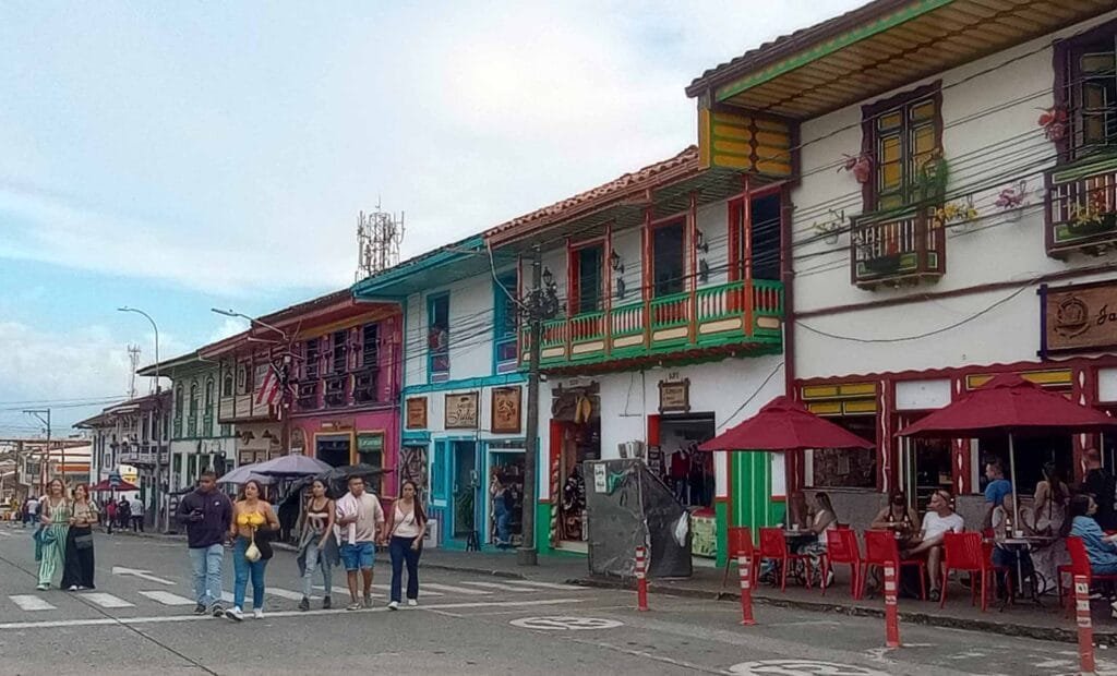 Calle céntrica de Filandia, Quindío, mostrando arquitectura colonial con balcones de colores, turistas caminando y personas en una terraza de café con sombrillas rojas.